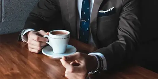 A man in suit and tie holding a cup of coffee.