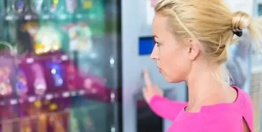 A woman in pink shirt touching the screen of a vending machine.