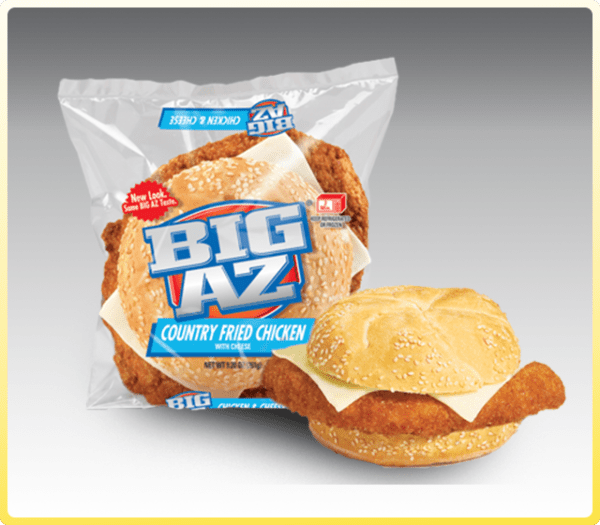 Plastic-wrapped BIG AZ Country Fried Chicken And Cheese Sandwich with new label, displayed beside an unwrapped version of the sandwich, all set against a plain background.