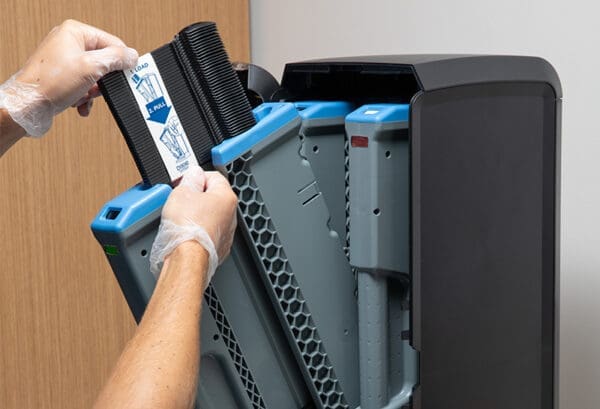 Hands wearing gloves replace a Dixie Ultra SmartStock Series-T Serving Spoon Refill in an air purifier unit, following instructions on a label.