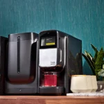 A Flavia® Chill Refresh for Creation 300 dispensing red liquid into a glass cup on a kitchen counter, with tea boxes and a plant beside it.