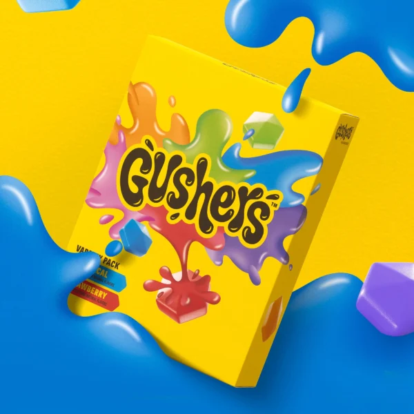 A vibrant Gushers Strawberry Splash and Tropical Flavors snack box with a colorful splash design, surrounded by fruit pieces and liquid splashes on a blue background.