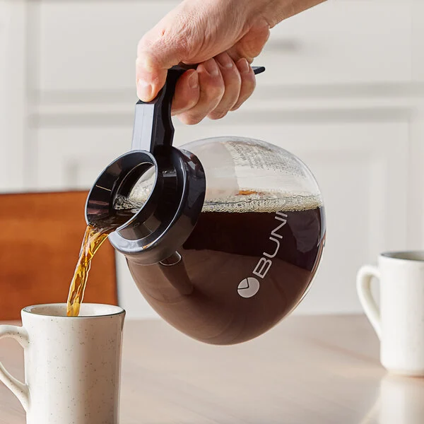 Hand pouring coffee from Bunn carafe.